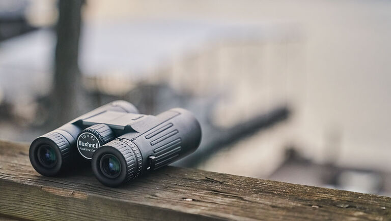 Bushnell Powerview 2 Binoculars sitting on a wooden railing at a waterfront